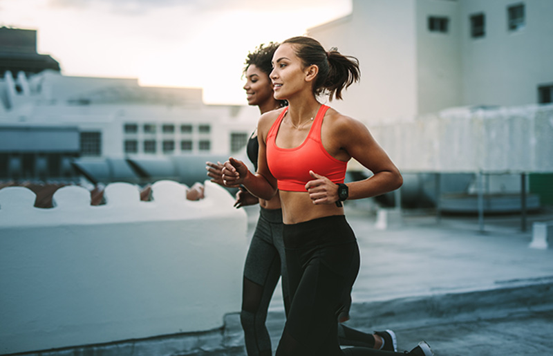 Two women jogging on a rooftop, with urban buildings in the background.