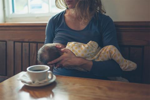 A mother cradles her sleeping baby in a cozy café, a cup of coffee resting on the table beside them.