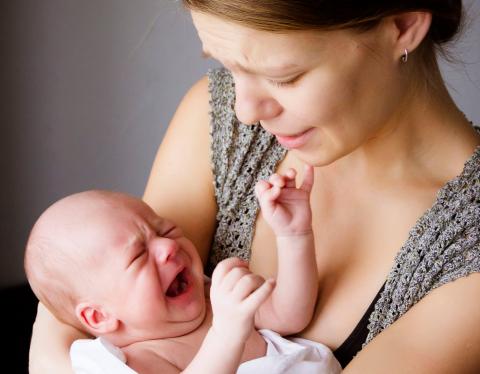 A mother gently cradles her baby, who is reaching out with tiny fingers. The background is softly lit, creating a warm atmosphere.