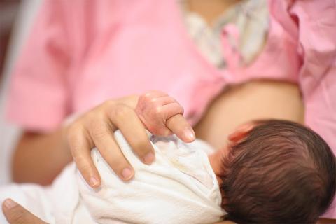 A mother cradles her newborn against her chest while breastfeeding, their hands gently touching in a moment of tenderness.