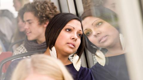 A group of passengers in a transit vehicle, some looking out the window, with blurred reflections on the glass.