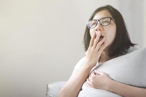 A person resting on a couch, holding a soft pillow and looking contemplative, with a neutral-colored wall in the background.
